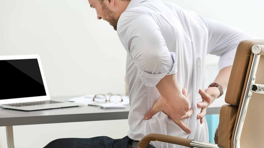 Homem sentado com dor nas costas mostrando a importância das empresas realizarem palestra de ergonomia para conscientização